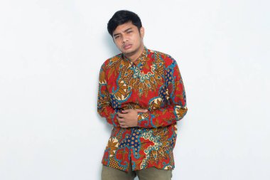 Batik giyen Asyalı adamın beyaz arka planda karnı ağrıyor.