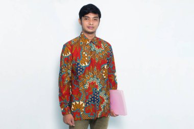 Beyaz arka planda pembe bir zarf tutarken Batik giyen Asyalı genç adam kendinden emin.