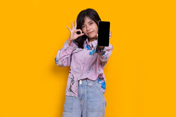 Young Beautiful Asian Woman Demonstrating Mobile Cell Phone Isolated Yellow — Stok fotoğraf