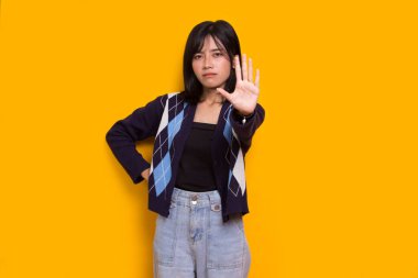 Eli açık genç bir kadın dur işareti yapıyor. Savunma jesti sarı arka planda.