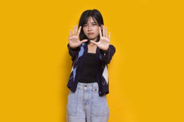 Eli açık genç bir kadın dur işareti yapıyor. Savunma jesti sarı arka planda.