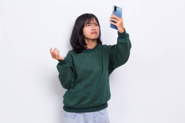 kızgın ve şok olmuş genç Asyalı güzel kadın beyaz arka planda izole cep telefonu kullanıyor.