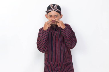 asian man with javanese traditional lurik cloth holding his nose because of a bad smelling isolated on white background