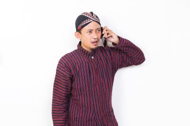Happy joyful asian man with javanese traditional cloth lurik using mobile smartphone isolated on white background