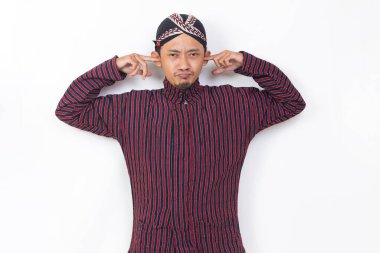 asian man with javanese traditional cloth lurik covering both ears with hands isolated on white background
