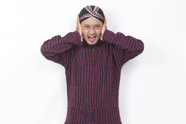asian man with javanese traditional cloth lurik covering both ears with hands isolated on white background