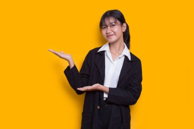 young asian woman pointing with fingers to different directions isolated on yellow background