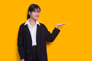 young asian woman pointing with fingers to different directions isolated on yellow background