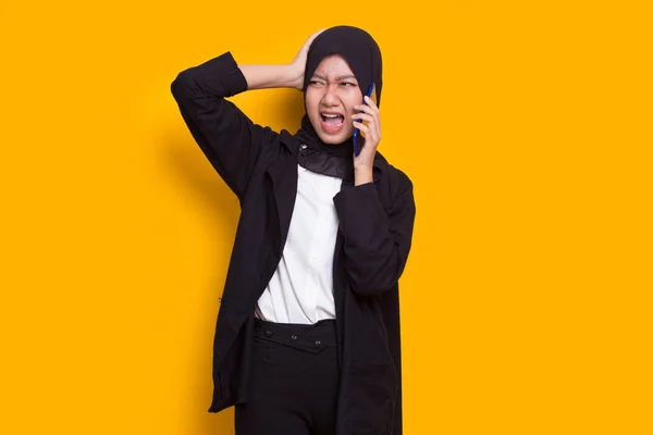 mad and shock young asian muslim business woman using mobile phone isolated on yellow background