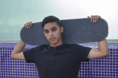 Genç Latin bir adamın kaykayla poz verirken yakın bir fotoğrafı. Kameraya bak..