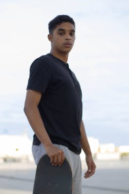 Latin adamın kaykayla poz verirken çekilmiş dikey fotoğrafı..