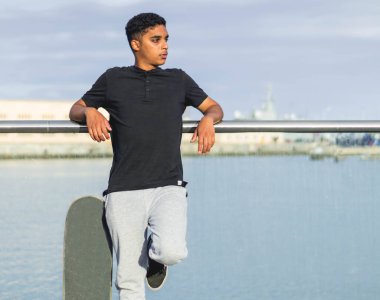 Skater boy resting next to his skate and the sea