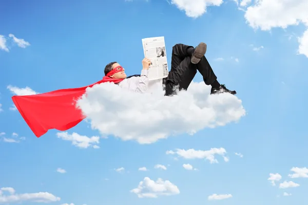 Male superhero lying on cloud and reading a newspaper — Stock Photo, Image