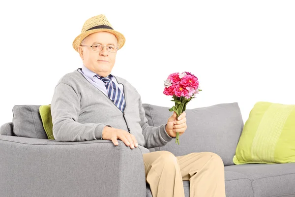 Senior on a sofa holding flowers — Stock Photo, Image