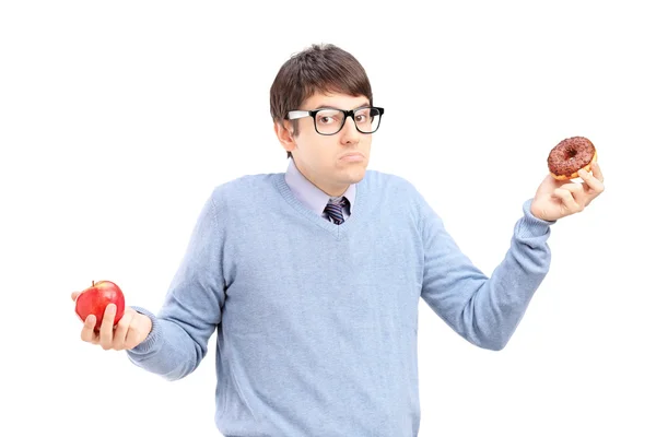Doubtful guy holding an apple and donut — Stock Photo, Image