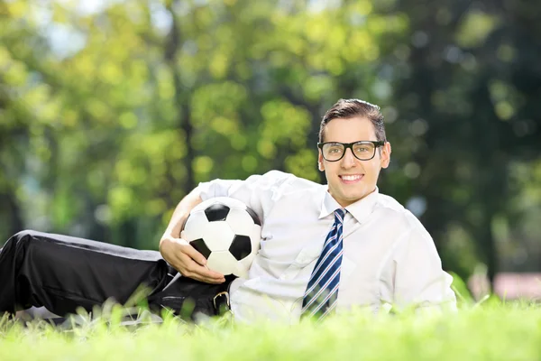 Homem segurando futebol e ograss deitado — Fotografia de Stock