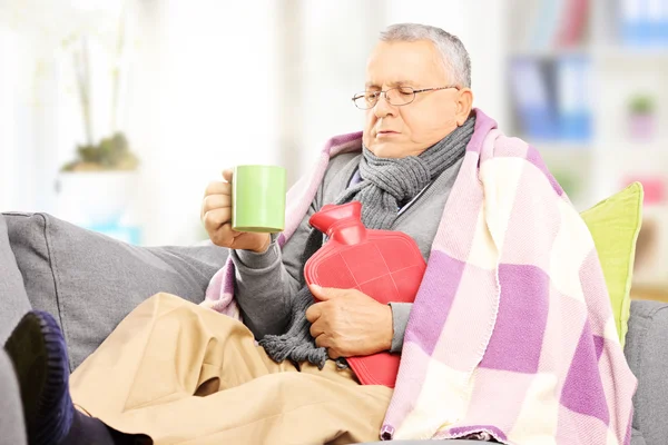 Hombre enfermo en el sofá bebiendo té caliente Imagen De Stock