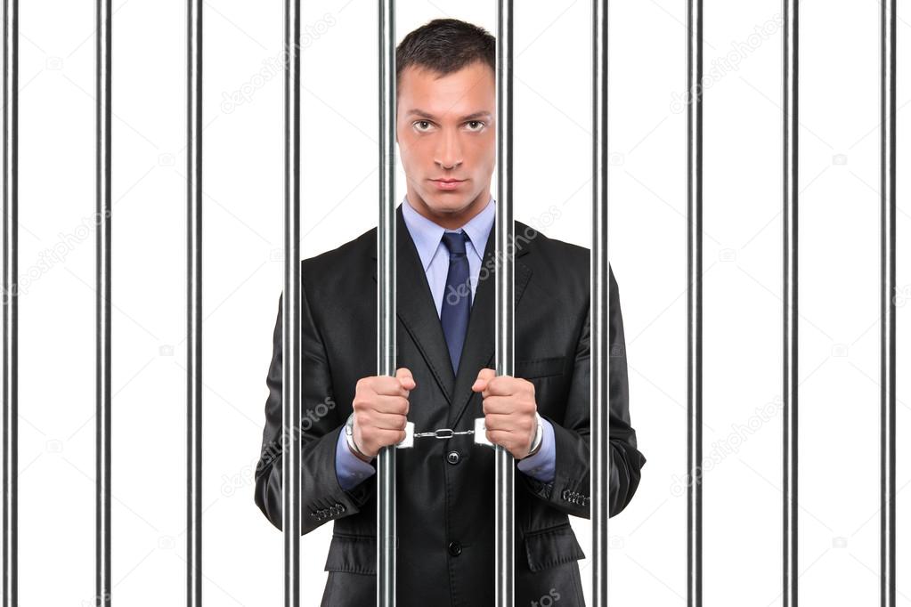 A handcuffed businessman in jail holding bars