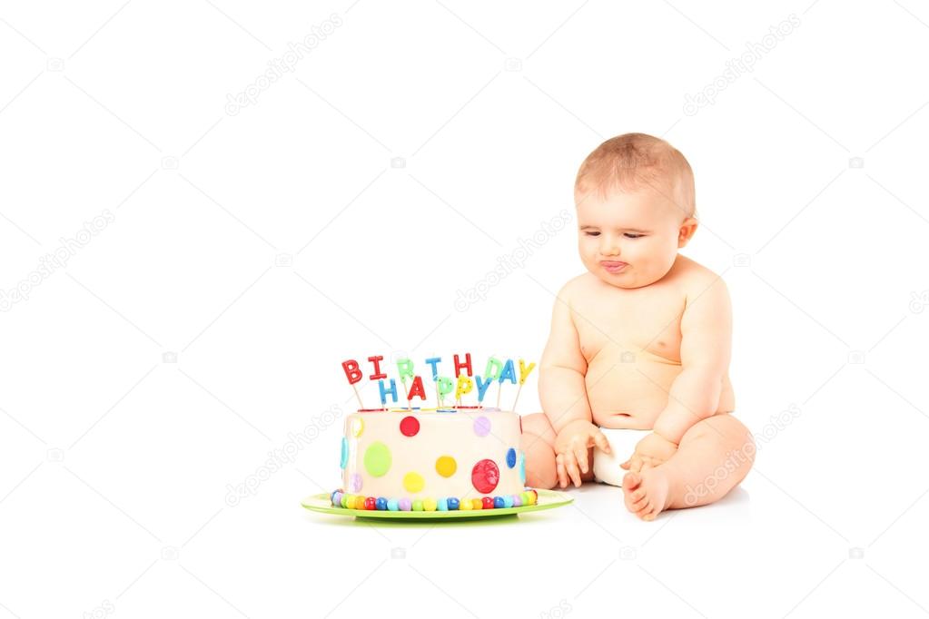 A 9 months old baby in diapers sitting next to a birthday cake Stock