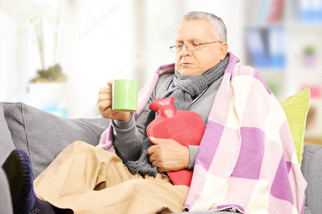 Ill man on sofa drinking hot tea