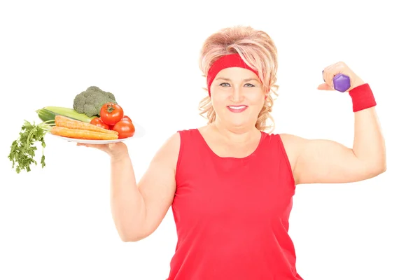 Женщина держит тарелку с овощами и гантелями — стоковое фото