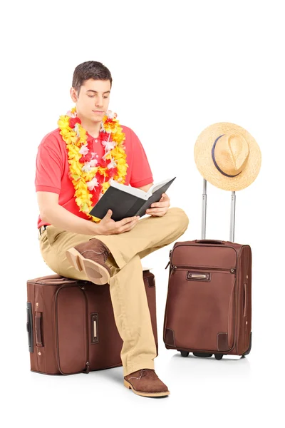 Male tourist reading book on briefcase — Stock Photo, Image