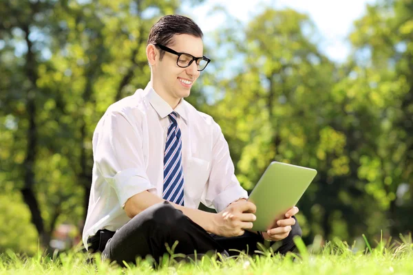 Jovem empresário trabalhando em um tablet em um parque — Fotografia de Stock