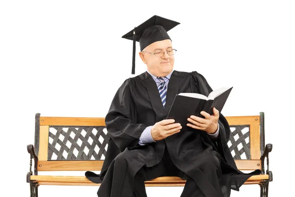 Mature man in graduation gown on bench — Stock Photo, Image