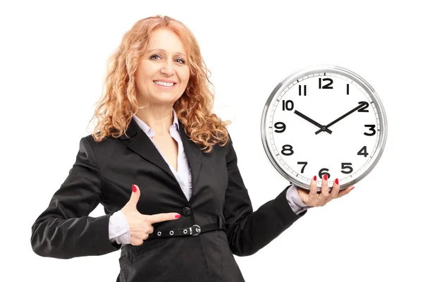 Una donna matura bionda in piedi e che punta su un orologio da parete Foto Stock