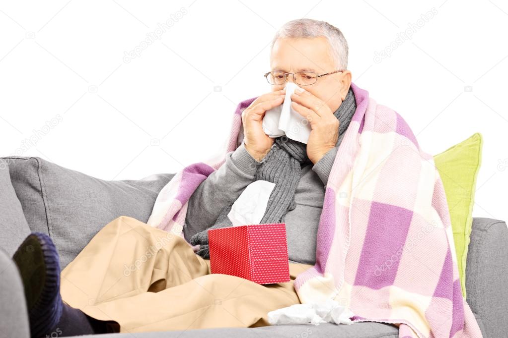 Senior man on a sofa blowing nose