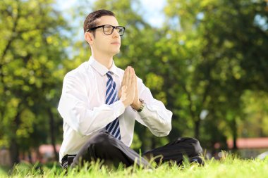 Businessman doing yoga exercise in park clipart