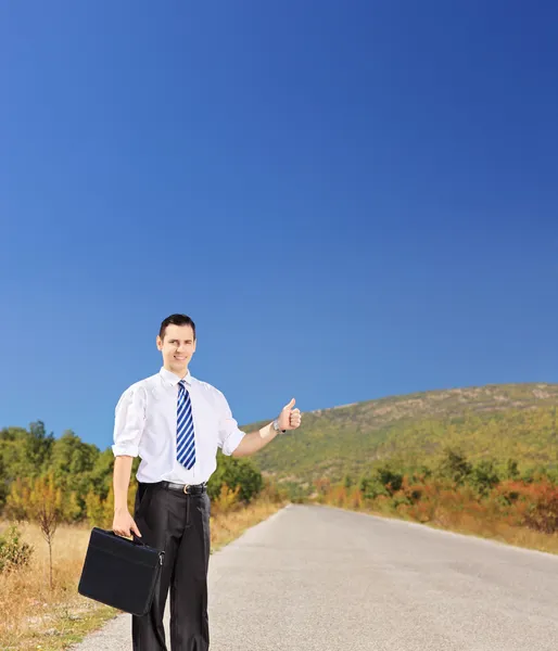 Businessperson hitchhiking on road — Stock Photo, Image