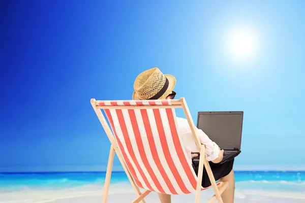 Kumsalda bir dizüstü bilgisayarda çalışan adam