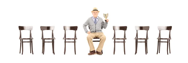 Man holding trophy seated on chair — Stock Photo, Image