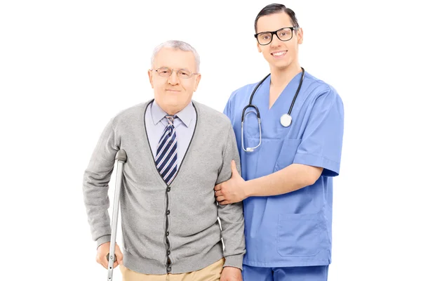 Jovem médico ajudando um senhor idoso com muleta — Fotografia de Stock