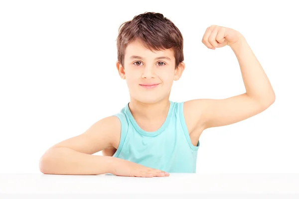 Ein Kind zeigt seine Muskeln auf einem Tisch sitzend — Stockfoto