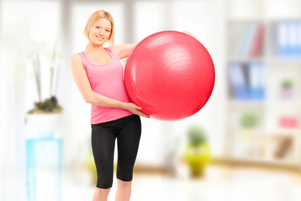 Blond female athlete holding a pilates ball and posing indoor — Stock Photo, Image