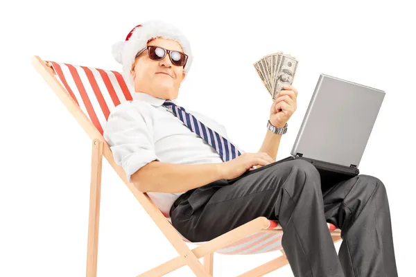 Mann mit Weihnachtsmütze, Geldscheinen und Laptop — Stockfoto