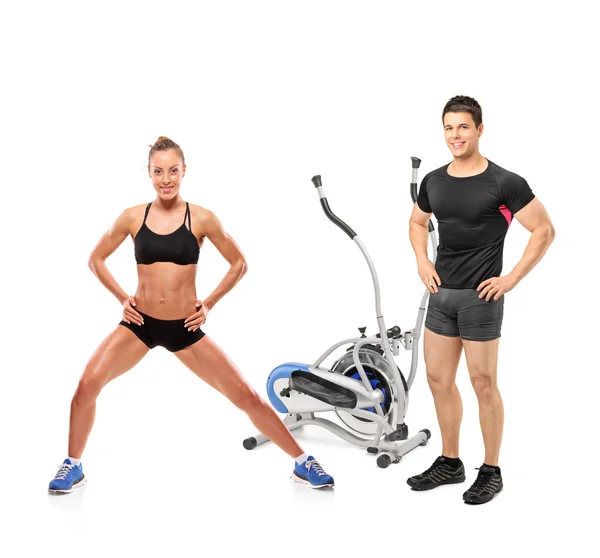 Female and male athletes posing next to a cross trainer machine — Stock Photo, Image