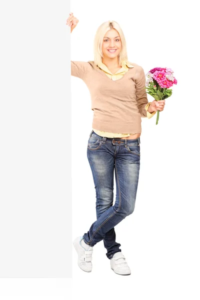 Mulher segurando flores ao lado de um painel em branco — Fotografia de Stock