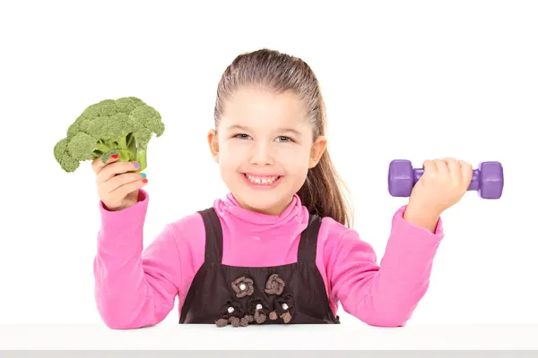 Girl holding broccoli and dumbbell — Stock Photo, Image