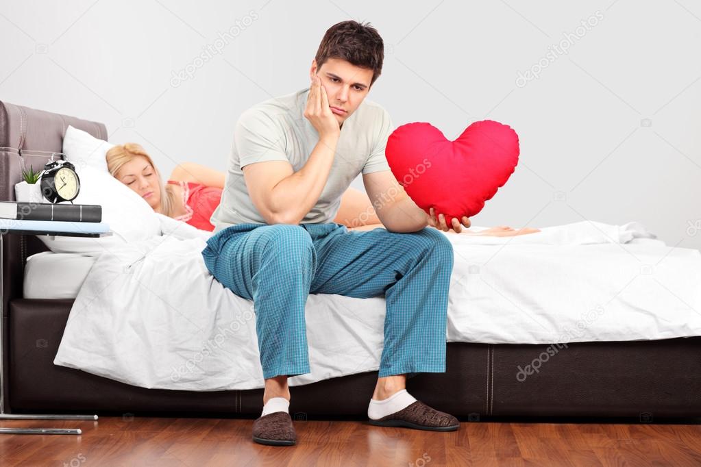Man in thoughts holding heart shaped pillow