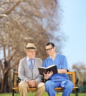 Nurse reading to pensioner in park