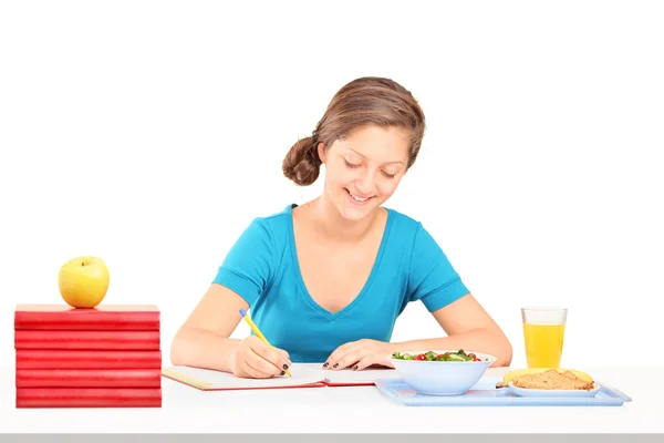 Dívka psaní domácích úkolů a jídlo — Stock fotografie