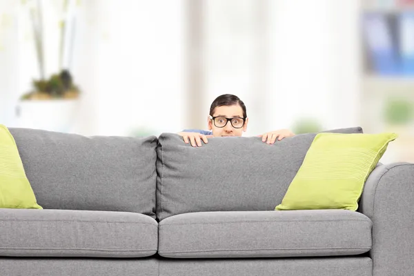 Homem assustado escondido atrás do sofá — Fotografia de Stock