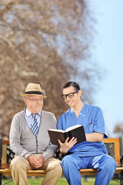 Sjuksköterska läsa pensionär i park — Stockfoto