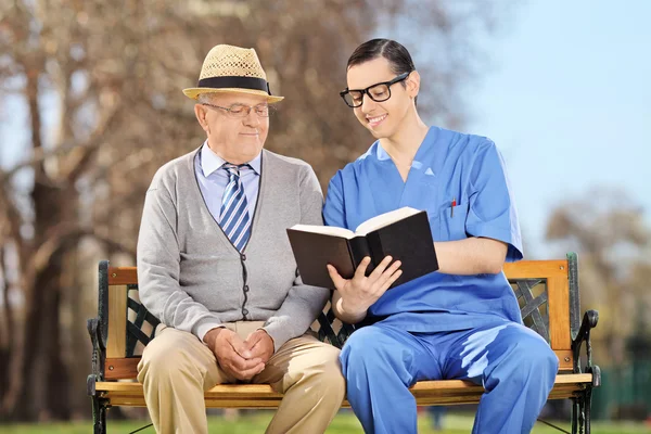 Sjuksköterska läsa pensionär i park — Stockfoto