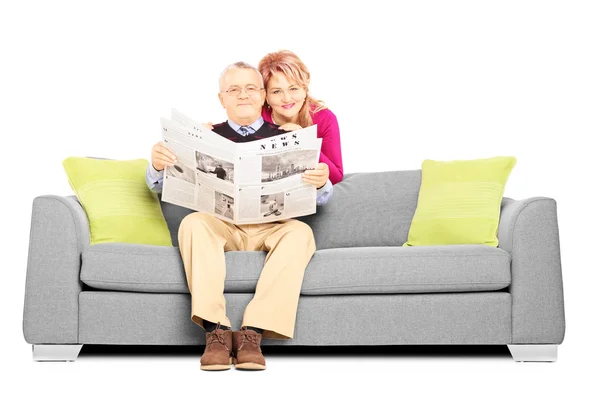 Couple with newspaper sitting on sofa — Stock Photo, Image