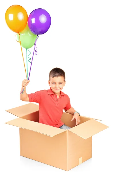 Niño en caja de cartón sosteniendo globos — Foto de Stock