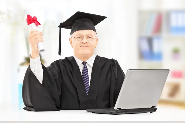 Reifer Mann im Abschlusskleid und Laptop — Stockfoto